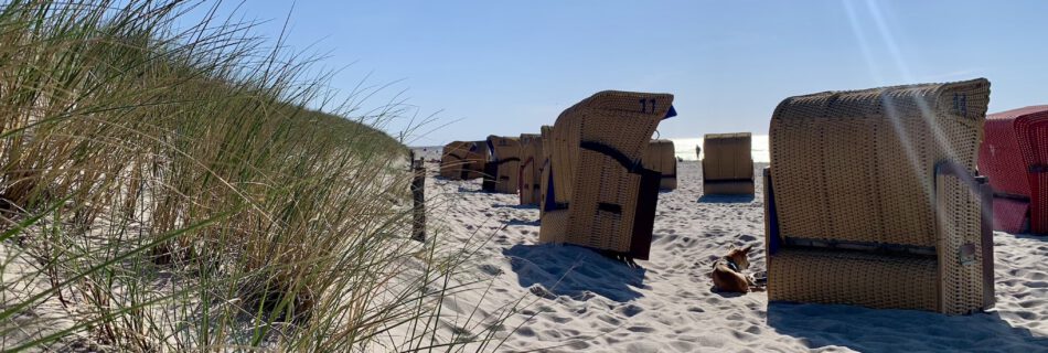 Sonniger Sandstrand mit Strandkörben und Dünen im Vordergrund, perfekt für plattdeutsche Veranstaltungen und gemütliche Treffen in maritimer Atmosphäre.